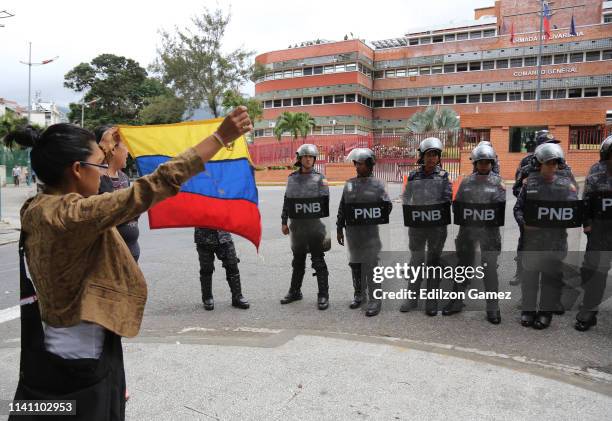 Woman waves a Venezuelan flag in front of members of the Venezuelan National Police during a protest at the Comandancia General de la Armada of San...