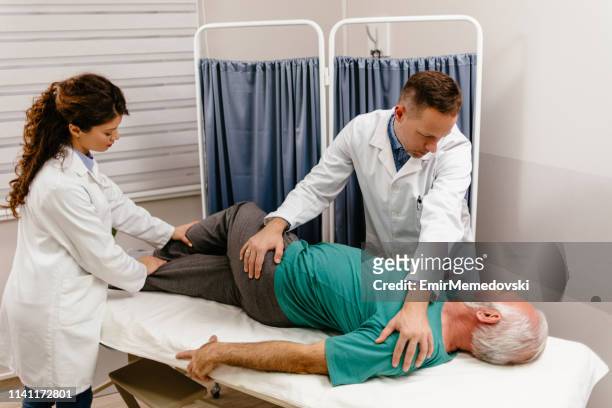 homme aîné ayant le dos examiné par un médecin - sciatic nerve photos et images de collection