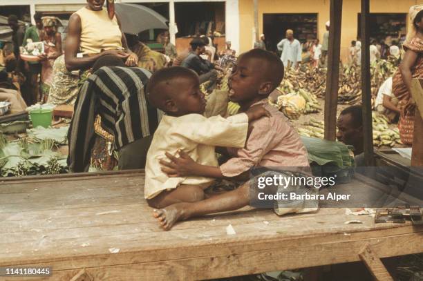 Two children playing near a market stall in Abidjan, Ivory Coast, February 1975.