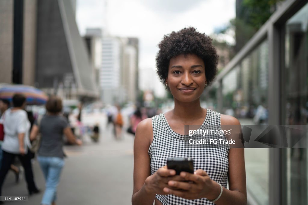 Mulher de negócios nova que usa o retrato móvel na cidade