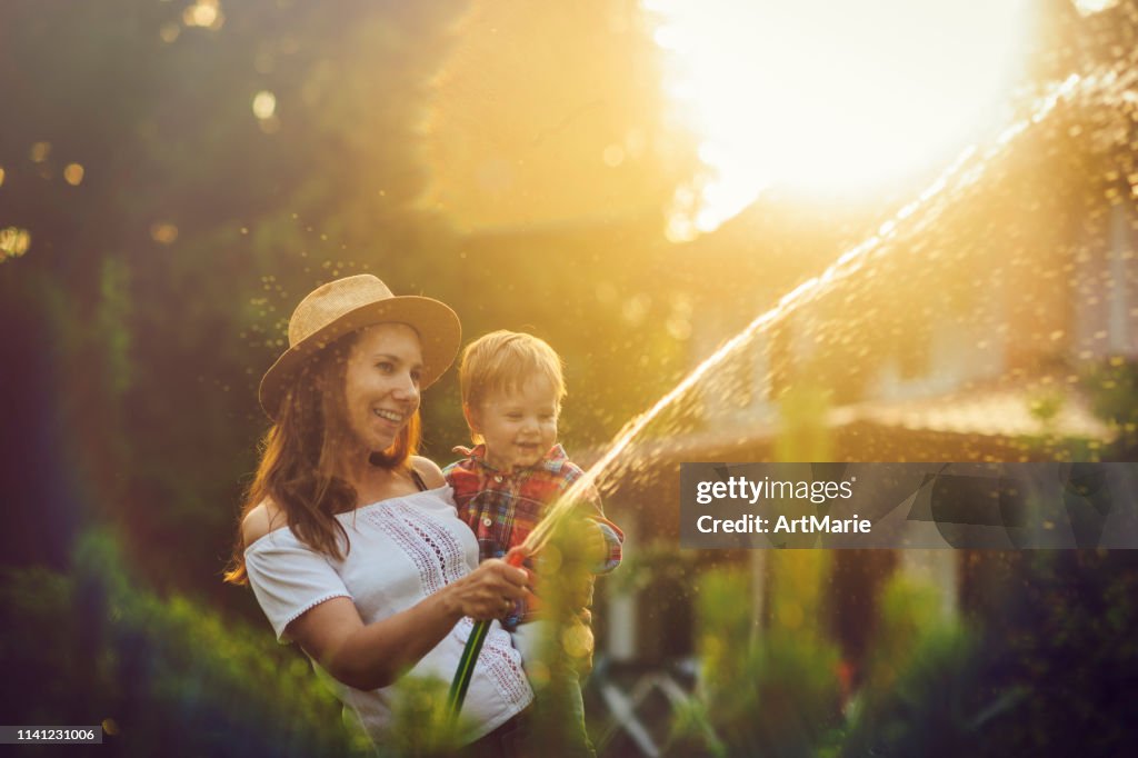 Mulher e seu filho que jardinam no jardim doméstico no por do sol