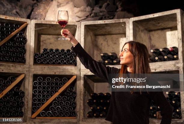 young girl looks color of wine by raising a glass against the light in the cellar. mese, valchiavenna, valtellina, lombardy, italy, europe. - sommelier stockfoto's en -beelden