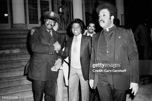 An unidentified New York City police officer shakes hands with American Soul and R&B singer James Brown while religious and Civil Rights activist...