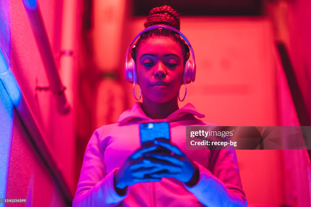 Porträt der jungen schwarzen Frau, die Musik unter Neonlicht hört