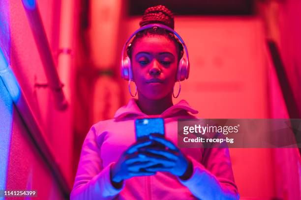 porträt der jungen schwarzen frau, die musik unter neonlicht hört - listening stock-fotos und bilder