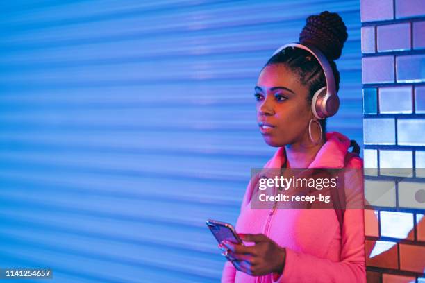 porträtt av ung svart kvinna som lyssnar på musik under neonljus - millennial pink bildbanksfoton och bilder