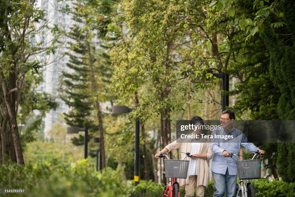 Asian Senior Couple Walking with Bicycle in Park
