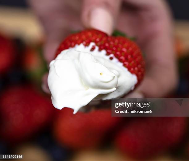 woman holding a strawberry with whipped cream - strawberries and cream stock pictures, royalty-free photos & images