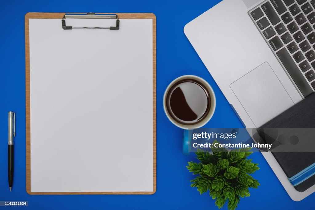 White Paper on Clipboard and Laptop on Blue Background