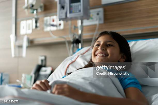 beautiful 9 year old girl lying down on hospital bed smiling - hospital bed stock pictures, royalty-free photos & images