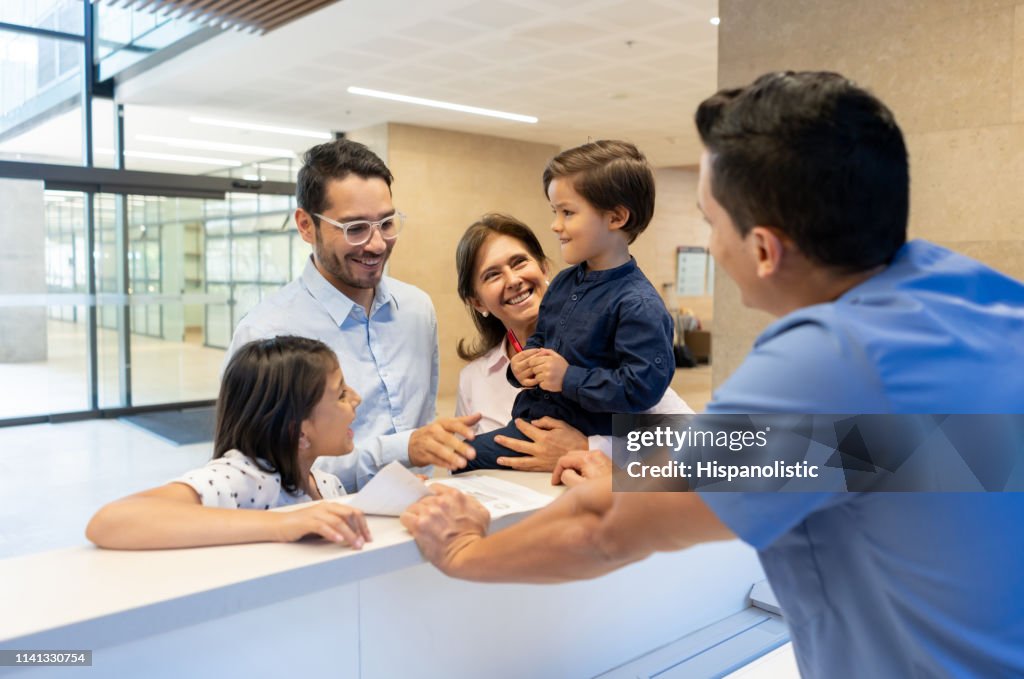 Vader met zijn kinderen en oma te registreren voor een consult met de kinderarts bij de receptie van de kliniek