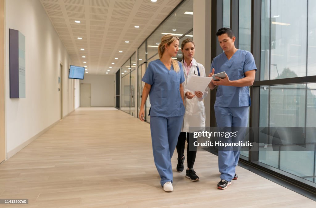 Medical residents showing something to female doctor on tablet while walking at the hospital