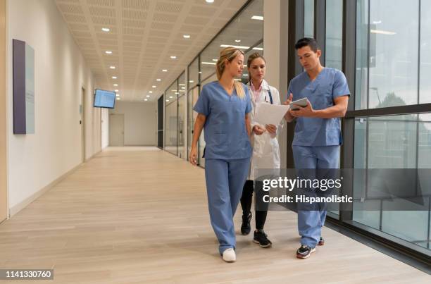 medical residents showing something to female doctor on tablet while walking at the hospital - civil imagens e fotografias de stock