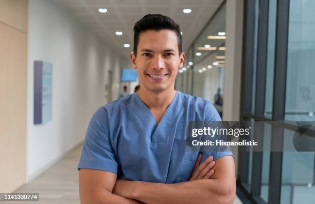 portrait of latin american male nurse at the hospital facing camera smiling with arms crossed - enfermeiro imagens e fotografias de stock