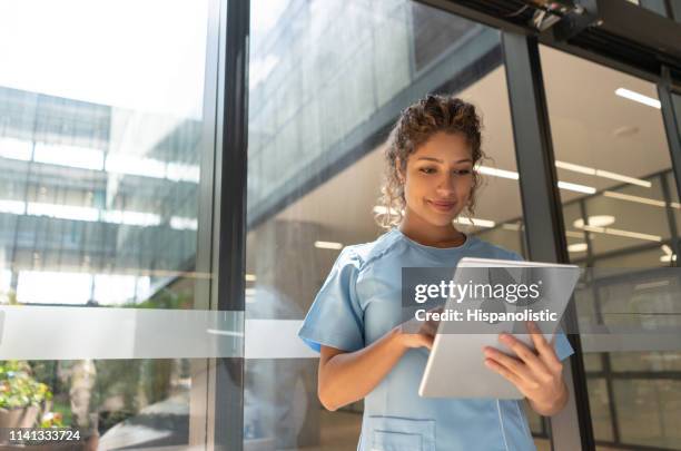 freundliche junge krankenschwester mit blick auf eine medizinische karte auf tablette leicht lächelnd - zivilist stock-fotos und bilder