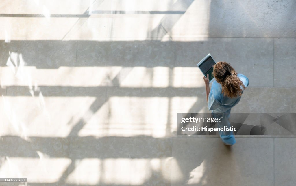 High angle view of nurse walking around hospital while looking at a medical chart on tablet