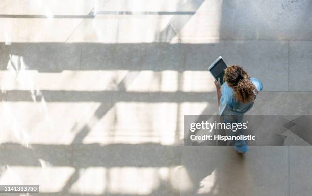 high angle view of nurse walking around hospital while looking at a medical chart on tablet - employee health stock pictures, royalty-free photos & images