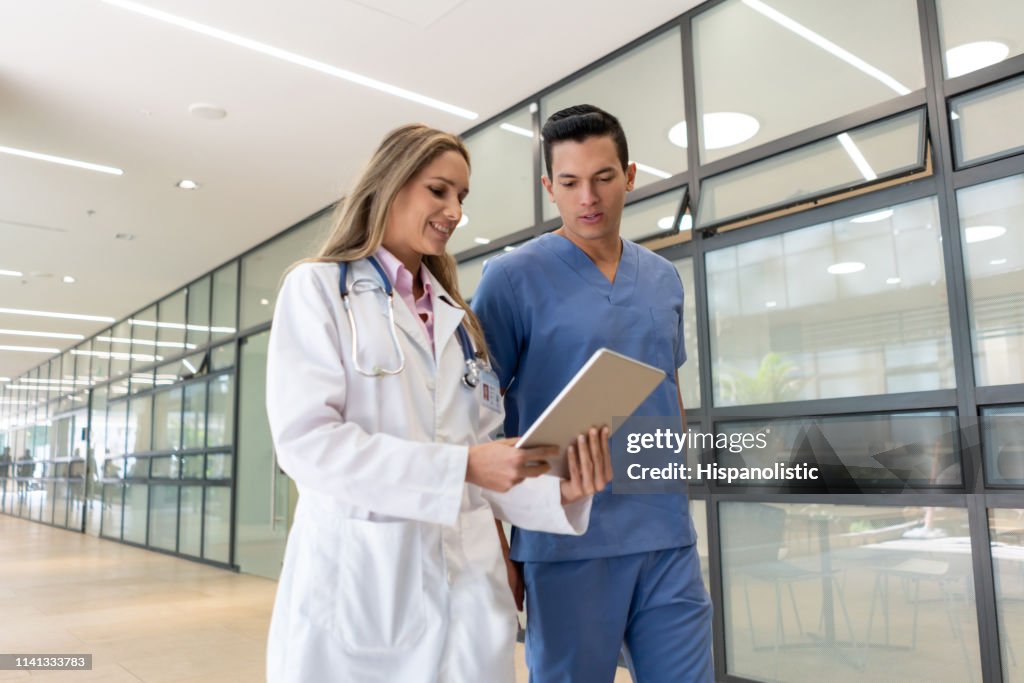 Hübsche Krankenschwester im Gespräch mit weiblichem Arzt, während beide auf eine Tablette zu Fuß durch den Flur
