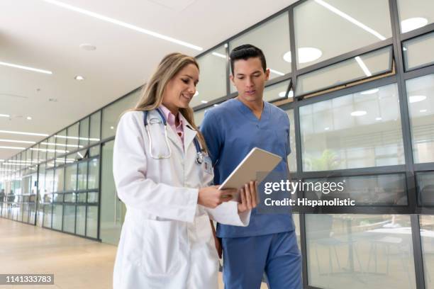 handsome male nurse talking with female doctor while both are looking at a tablet walking through the corridor - civil imagens e fotografias de stock