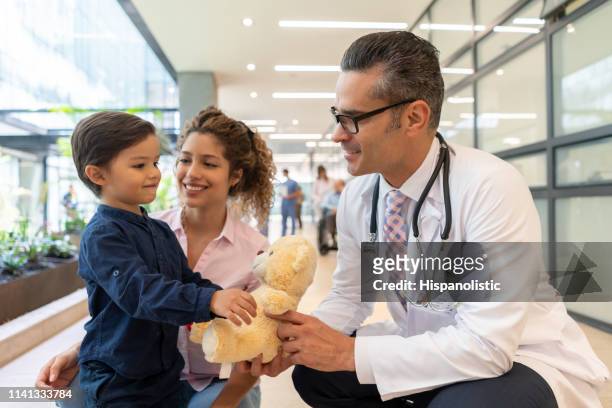 sweet little boy with his mom showing his teddy bear to pediatrician all smiling very happy - family pediatrician stock pictures, royalty-free photos & images