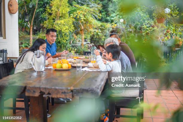 smiling multi-generation family eating together - chinese eating backyard stock pictures, royalty-free photos & images