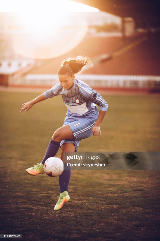 Determined female soccer player practicing with ball on the field.