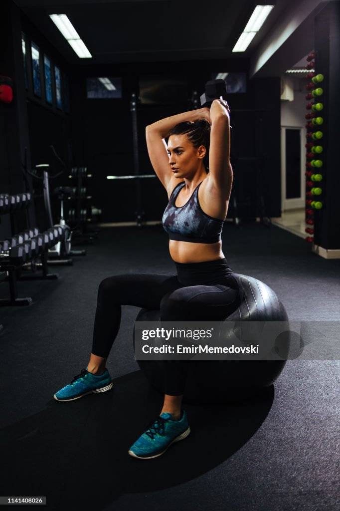 Retrato de la hembra haciendo ejercicios con mancuerna en el gimnasio