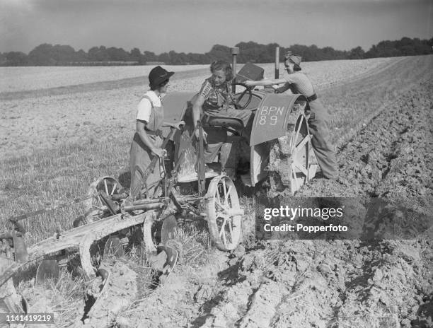 View of three female workers from the Women's Land Army operating a tractor and plough on Gertrude Denman's farm and estate in Sussex, England soon...