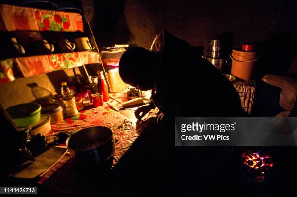 Young woman preparing food by a gas lantern in her hut in Sani Pass, Lesotho, Africa.