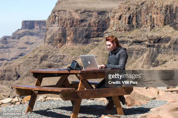 Young woman working on her laptop at a picnic table in the mountains of Lesotho, Africa.