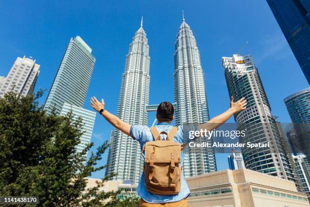 rear view of tourist with backpack spreading arms to kuala lumpur skyline with petronas towers - petronas towers stock-fotos und bilder