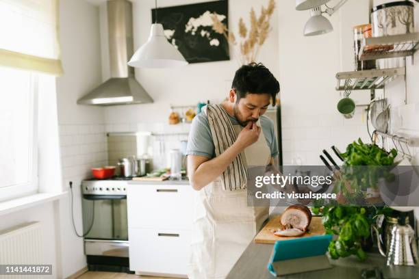 asian man making chashu pork with the help of digital cookbook - cooking at home stock pictures, royalty-free photos & images