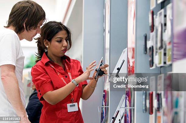 Vodafone employee Vish Bhowmick, right, shows a mobile phone handset to a customer at one of the company's stores in London, U.K., on Friday, May 13,...