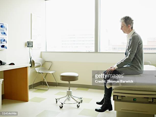 female patient sitting on exam table in exam room - examining table stock pictures, royalty-free photos & images