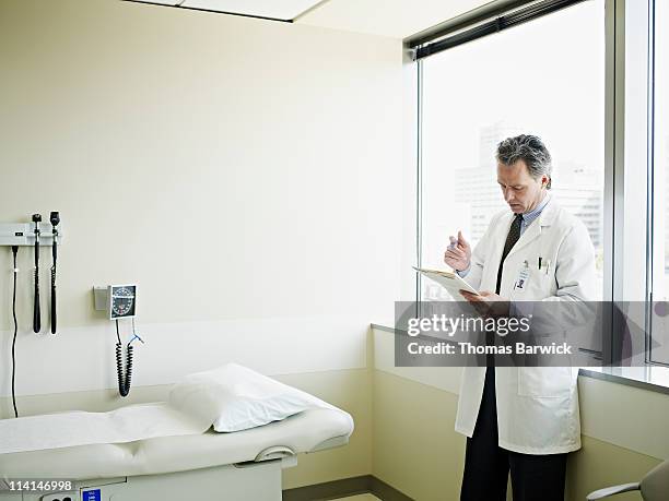 male doctor examining patient chart in exam room - examination room fotografías e imágenes de stock