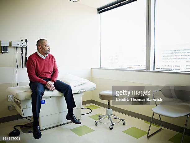 male patient sitting on exam table in clinic room - man waiting foto e immagini stock