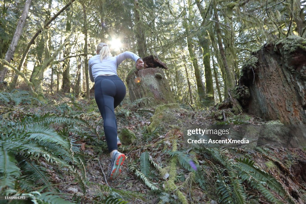 Female trail runner ascends through forest, without path
