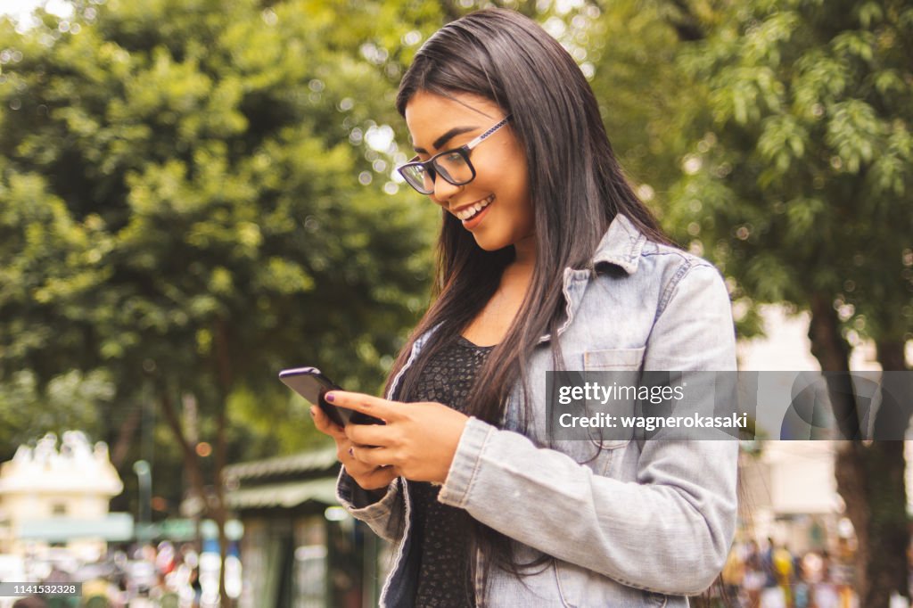 Retrato de uma menina brasileira que usa o smartphone que olha a tela do dispositivo