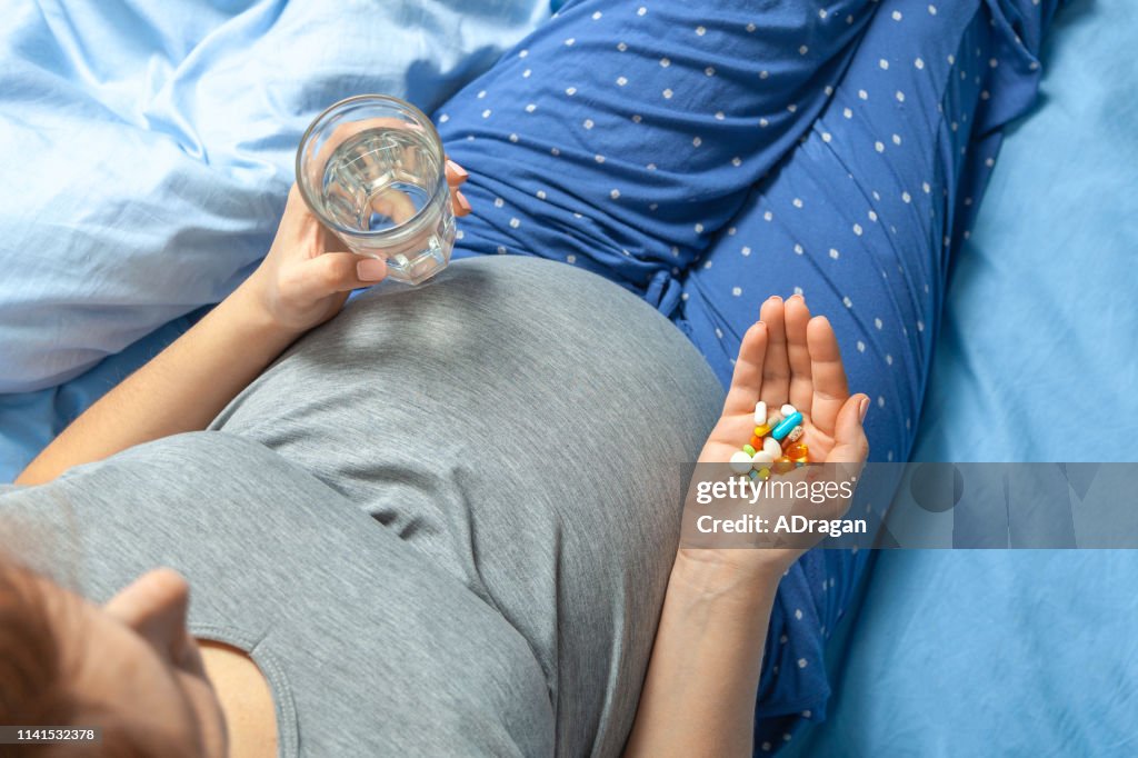 Pregnant woman with stomach and holding in her hands and pills and glass of water. Treatment of pregnant women.