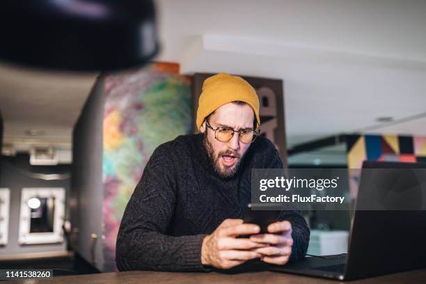 hipster entrepreneur shocked by the news - mobile bad news stock pictures, royalty-free photos & images