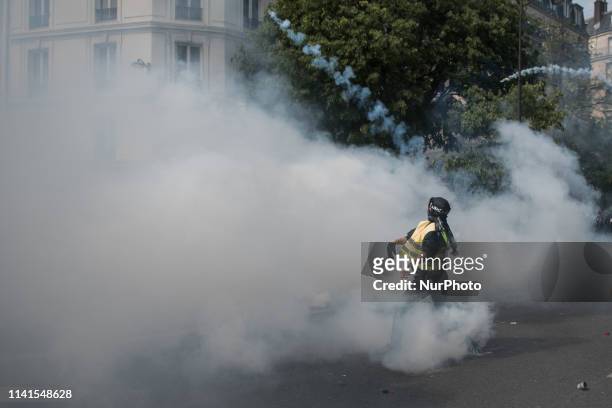 Yellow vest with a covered face throws a tear gas at the police. Paris, 1 May 2019. Un gilet jaune avec le visage couvert lance un gaz lacrymogène à...