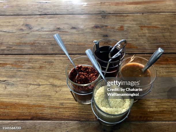 a set of four traditional thai condiments for on a wooden table : sugar (sweet), fish sauce (nam pla - salty), dried chilli  (spicy), and seafood sauce (spicy and sour). - nuoc cham stock pictures, royalty-free photos & images