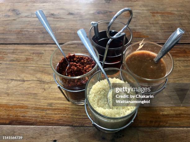 a set of four traditional thai condiments for on a wooden table : sugar (sweet), fish sauce (nam pla - salty), dried chilli  (spicy), and seafood sauce (spicy and sour). - nuoc cham stock pictures, royalty-free photos & images