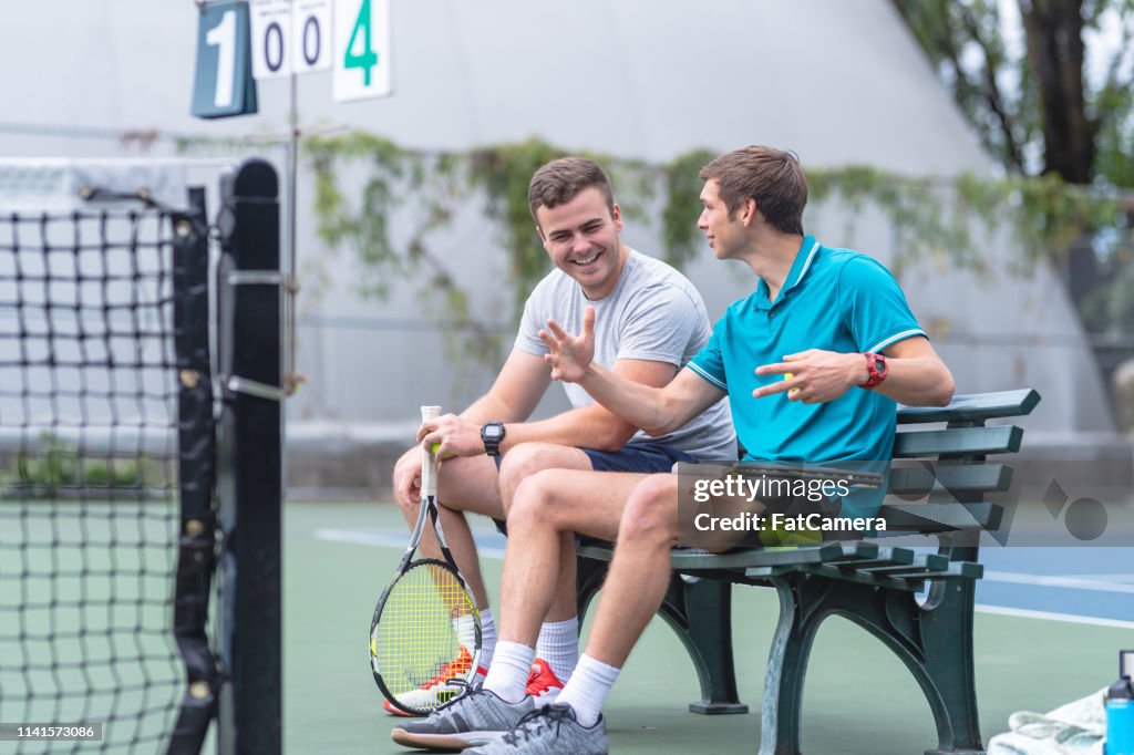 Two males relax on a bench after playing a tennis match