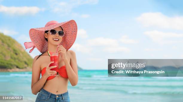 the girl is smiling in bikinis and sunglasses with watermelon juice on the beach. - melone hut stock-fotos und bilder