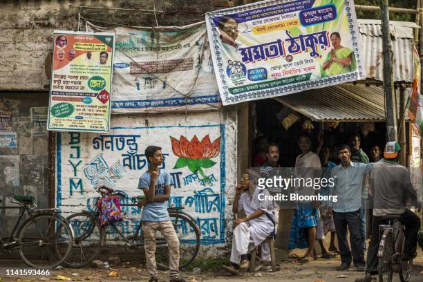 People stand near campaign banners for All India Trinamool Congress party, right, and Bharatiya Janata Party left, in Swarupnagar, West Bengal,...