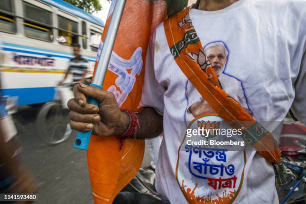 Man wearing a shirt featuring India's Prime Minister Narendra Modi carries a Bharatiya Janata Party flag during a campaign rally in Maslandapur, West...