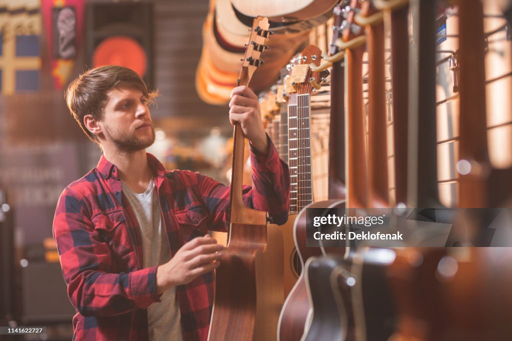 A young man choosing a guitar in a store