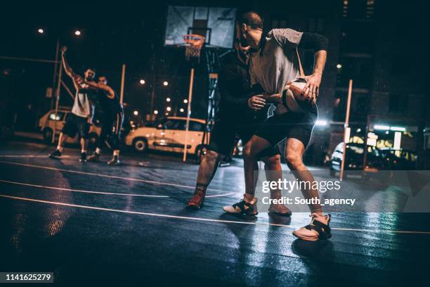 friends playing basketball downtown at night - streetball stock pictures, royalty-free photos & images