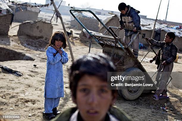 Young Afghan refugees from Kandahar play with an abandoned and unused push cart amid refuse and debris in a squalid camp on December 17, 2009 on the...
